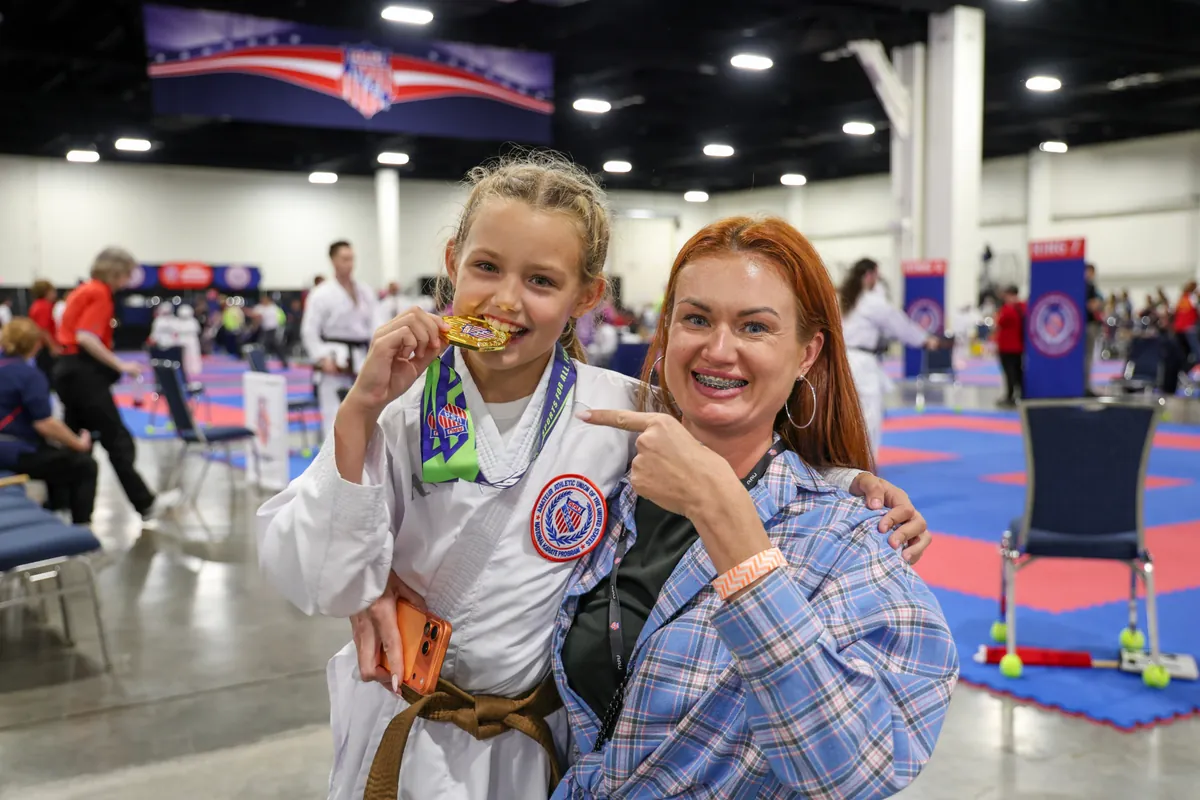 Karate athlete Dominika Tsybina biting her AAU national gold medal next to her mom